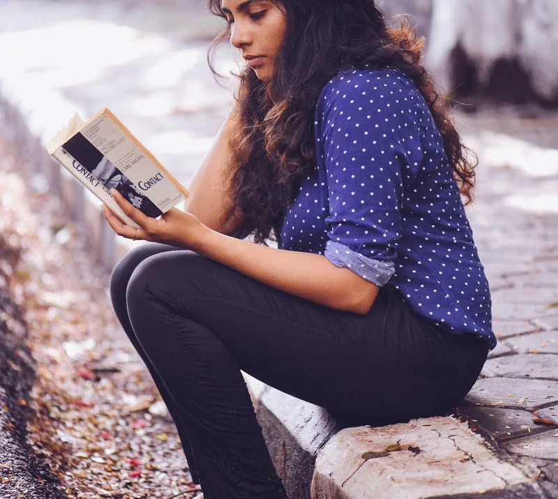A young woman reading a book on a kerb.
