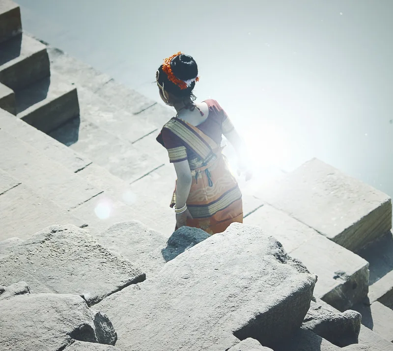 A woman walking down the stone steps of a stepwell in sunlight.