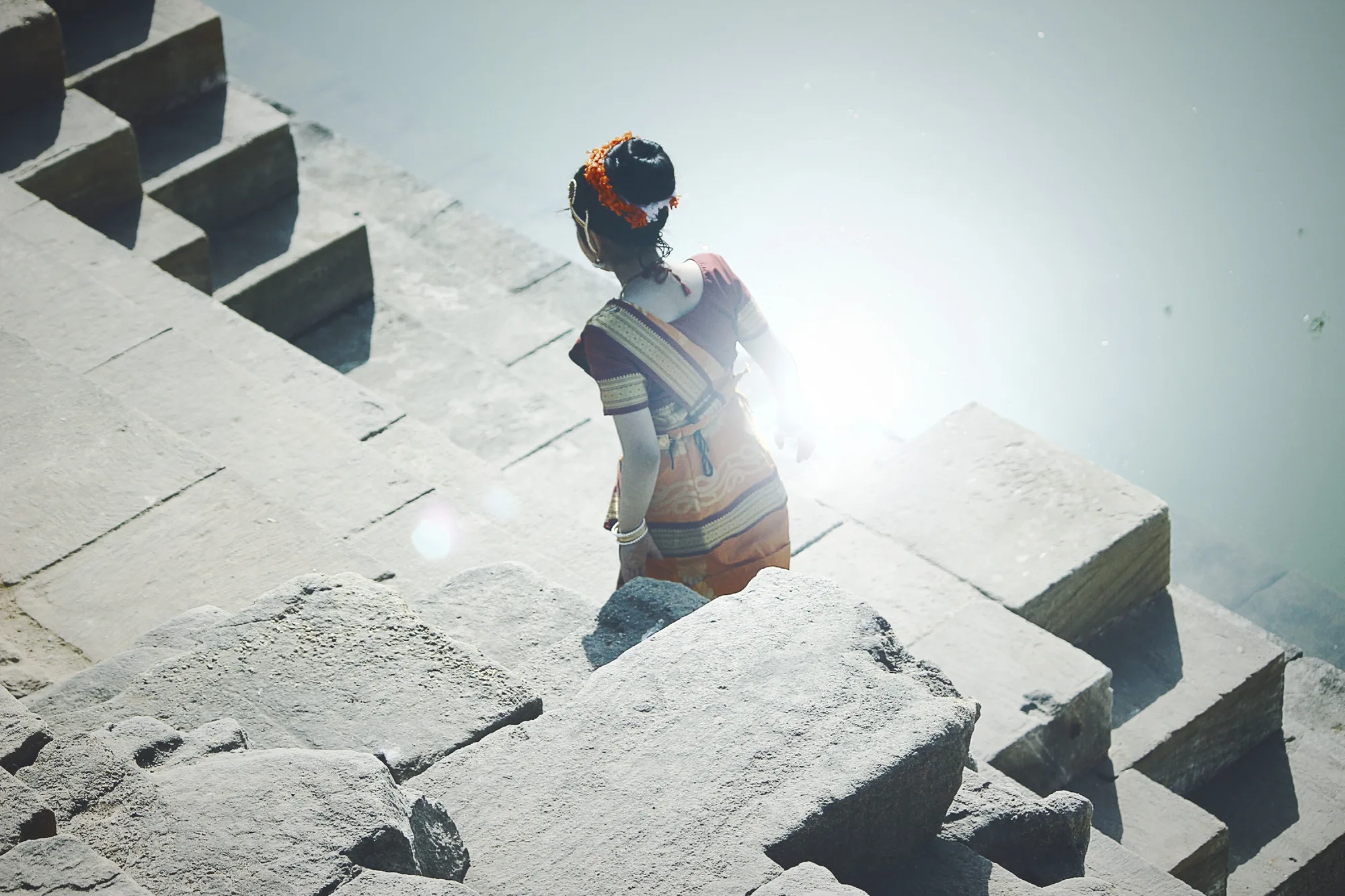 A woman walking down the stone steps of a stepwell in sunlight.